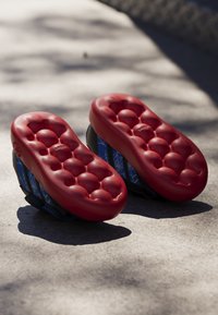 Red cushioned soles with bubble-like texture, featuring blue spider web patterns on the sides, designed for comfort and support.