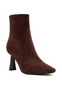 Stivale alla caviglia in suede marrone con punta affusolata e tacco sottile. Presenta una texture liscia e dettagli di cucitura minimali.