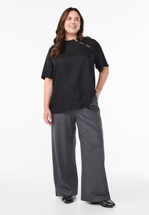 Top negro de manga corta con detalle de corte lateral, combinado con pantalones de cuadro grises de pierna ancha y mocasines negros. Atuendo simple y casual.