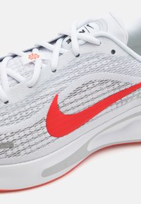Nike løpesko med hvit mesh overdel, rød logo og grå detaljer. Har en polstret såle og intrikat vevd tekstur.