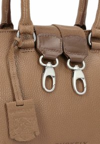 Sac à main en cuir brun texturé avec des clips en métal argenté doubles, une étiquette décorative et des coutures contrastées.