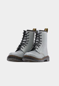 Ζευγάρι γυαλιστερά ασημένια μποτάκια με κορδόνια, μαύρες σόλες, πορτοκαλί ραφές και επώνυμα ταιριάσματα στην πλάτη σε λευκό φόντο.