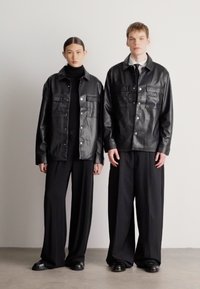 Melnas ādas jaku ar pogām un krūšu kabatām komplekts ar melniem zemām kakla džemperiem un plašu kāju biksēm. Gluda tekstūra, minimālistisks dizains.
