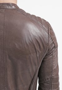 Prime piano di una giacca di pelle marrone usurata che mostra cuciture dettagliate e un design imbottito sulle spalle nella parte superiore della schiena e del braccio.