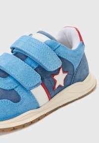 Baskets en daim bleu avec des accents blancs et rouges, dotées de bandes velcro, d'un détail en étoile et d'une semelle texturée pour une meilleure adhérence.