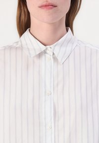 White button-up shirt featuring light blue vertical stripes, a classic collar, and pearlescent buttons on a smooth, lightweight fabric.