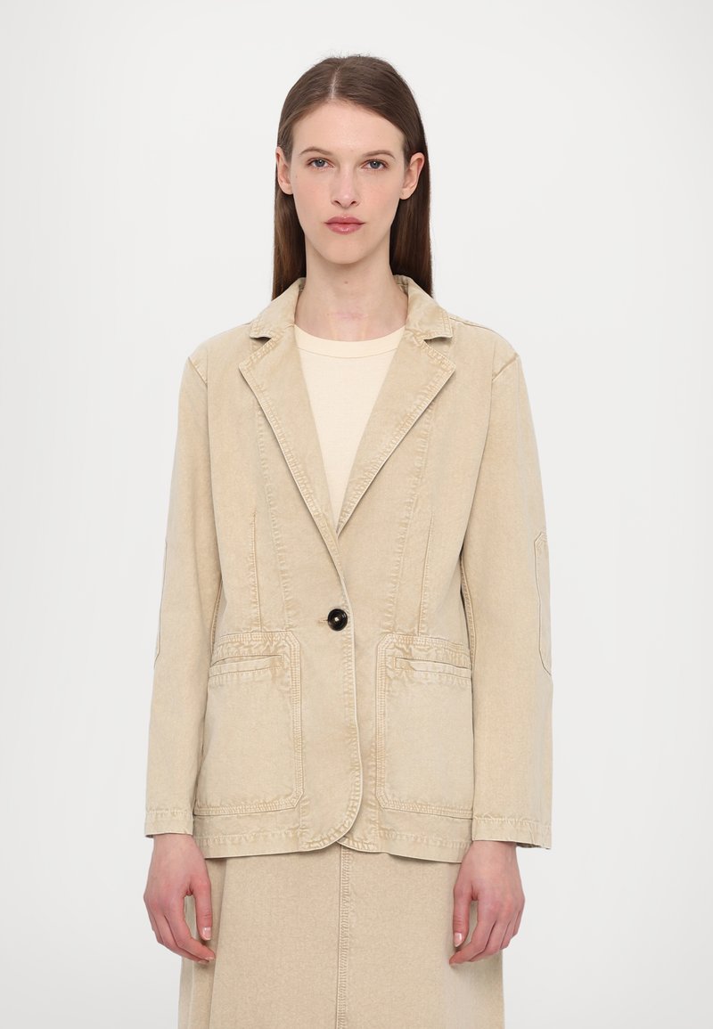 Beige denimblazer, enkel svart knapp, två framfickor, strukturerad slag, något skräddarsydd passform, långa ärmar, rena sömnadsdetaljer.