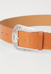Tan leather belt with silver floral-engraved buckle. Features a smooth texture, multiple holes for adjustment, and a minimalist design.
