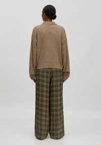 Beige breiwol trui met afhangende schouders, gecombineerd met groen geruite wijde broek met oranje accenten. Zachte textuur en relaxte pasvorm.