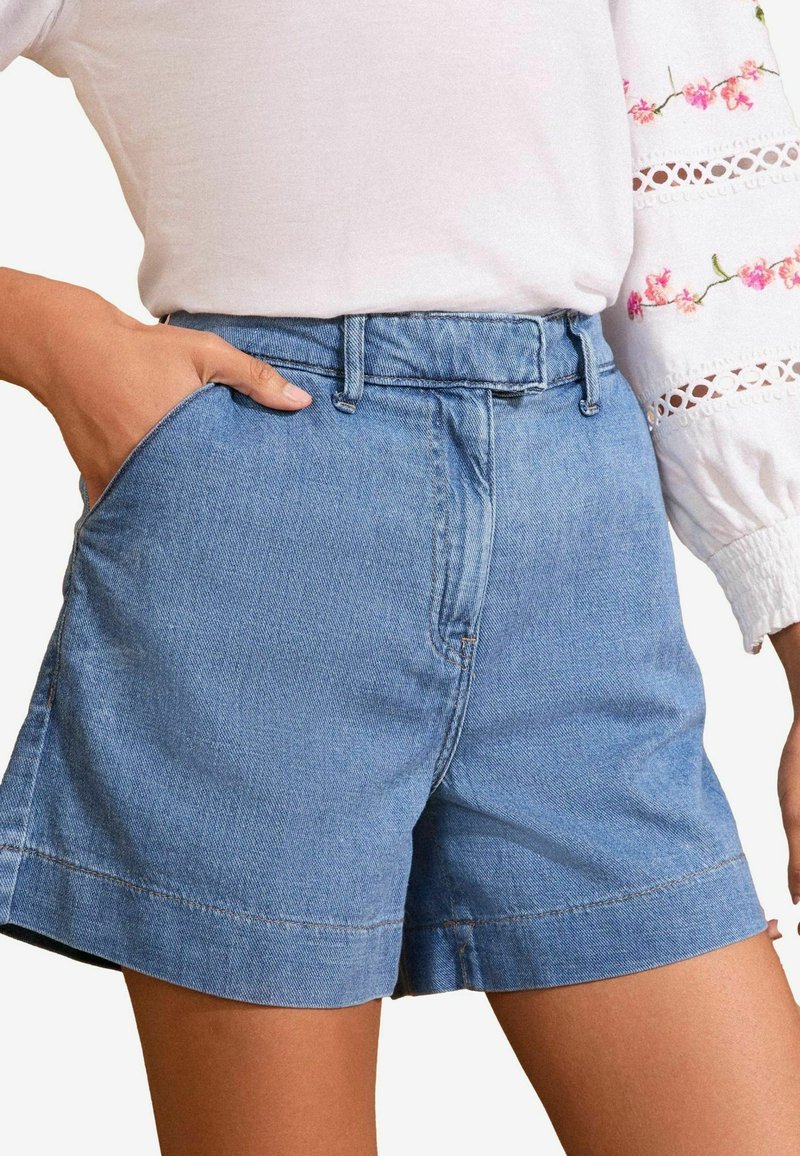 Traper sortsi u svijetloplavoj boji, s klasičnim dizajnom od pet džepova, šivenim rubom i pojasom. Meka tekstura s opuštenim krojem.