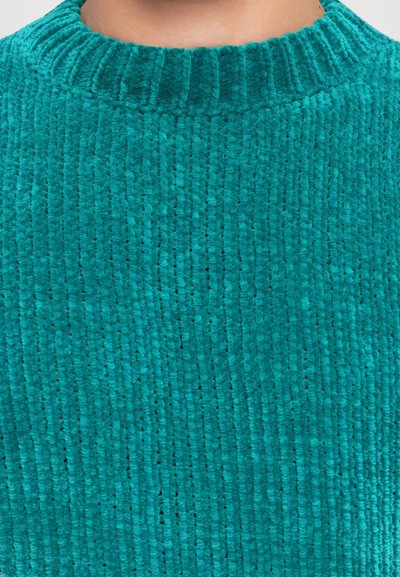 Close-up of teal ribbed knit sweater fabric and neckline on a person’s upper chest and neck.