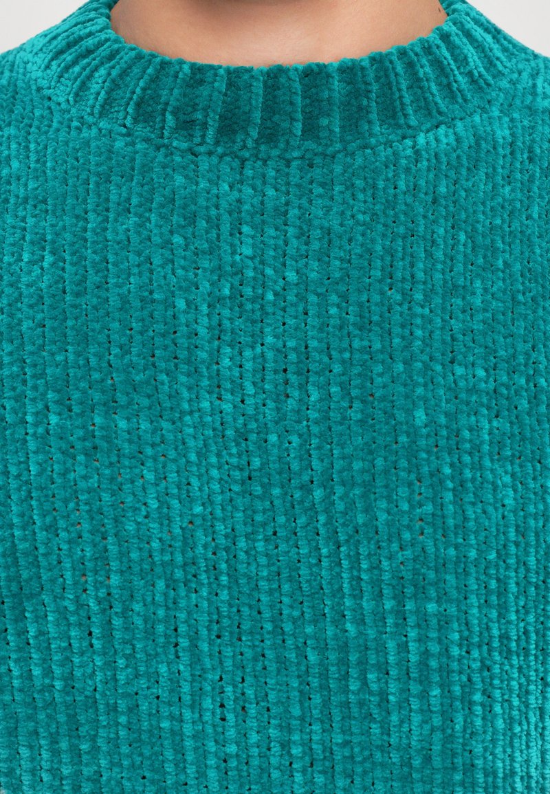 Close-up van een teal ribbelgebreide trui stof en de halslijn op de bovenste borst en hals van een persoon.
