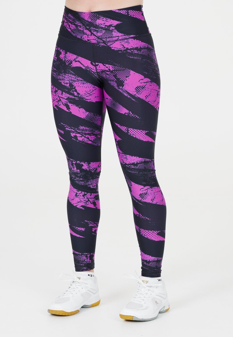 Ben med högmidjade svarta leggings med livliga lila abstrakta mönster, tillsammans med vita sportskor med gummisålar.