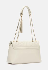 Prošívaná krémová kabelka z umělé kůže se zlatým řetízkovým uchopem, vyznačující se klopovým uzávěrem a dekorativním třásním.