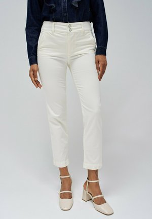 Pantalones de algodón blancos con un diseño de pierna recta, dos bolsillos frontales y cierre de doble botón. Llevados con zapatos de tacón bloque beige.