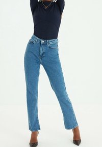 Jean en denim bleu taille haute avec une coupe droite, doté d'une fermeture classique à boutons et fermeture éclair, cinq poches, et un effet délavé.