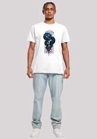 Hvit bomull T-skjorte med et grafisk trykk av en slange og en panter, med detaljer i blått, svart og lilla; brukt med lys denim og hvite sneakers.
