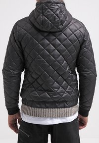 Czarna pikowana kurtka z kapturem, z teksturowanym wzorem w romby oraz prążkowanym szarym pasem w talii i na mankietach. Materiał wydaje się błyszczący i gładki.