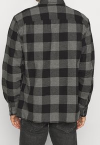 Svart och grå rutigt flanellskjorta, med knapp-ned krage, långa ärmar och rak fåll. Mjuk textur med ett klassiskt rutmönster.