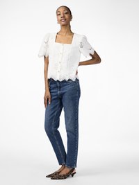 White puff-sleeve blouse with square neckline and button closure; intricate eyelet pattern; paired with blue high-waisted jeans and leopard print heels.