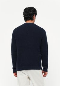 Marineblauwe gebreide trui met een gestructureerde stof, geribde manchetten en tailleband. Ontworpen voor een ontspannen pasvorm met een ronde hals.