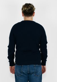 Maglione a coste navy con maniche lunghe e scollatura rotonda. Indossato con jeans blu, mette in risalto un design aderente e un tessuto texturizzato.