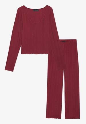 Rotes Langarmshirt mit gewelltem Saum und Ausschnitt, kombiniert mit langen Hosen in lockerer Passform aus strukturiertem Rippstoff.