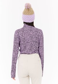 Top de manga larga morado con un estampado de leopardo negro, combinado con pantalones beige claros. Un gorro de punto en crema y lavanda con un pompón.
