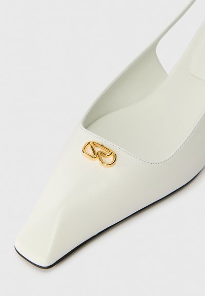 Bílé kožené slingback boty s špičatou špičkou, s akcentem zlatého dvojitého kruhového loga na nártu a hladkým, matným povrchem.