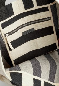 Canvas tas met zwarte en crèmekleurige horizontale strepen, voorzien van een ritszak en een gestructureerde geweven afwerking.