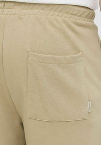 Shorts en coton beige avec une surface texturée, une taille élastique et une poche arrière avec une étiquette de marque.