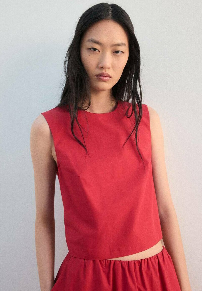 Haut rouge sans manches en coton, avec une coupe ajustée, un col rond et une longueur courte. Texture lisse et silhouette simple.