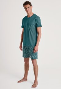 Teal katoenen t-shirt met korte mouwen en een borstzak, gecombineerd met geprinte shorts met spiraalpatronen in groen en wit.