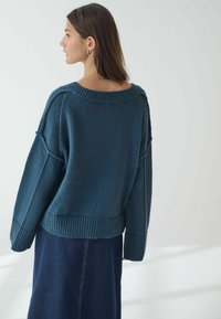 Teal stickad tröja med en bred båtkrage, sänkt axelparti och ribbade ärmslut och fåll. Matcher med en mörk denimkjol.
