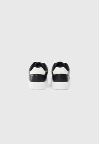 Adidași alb-negru cu un finisaj din piele netedă, având un panou din spate texturat de culoare albă, talpă albă și branding subtil pe călcâi.