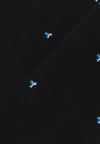 Černá textilie s pleteným vzorem a malými modrými a bílými geometrickými tvary rovnoměrně rozloženými po povrchu.