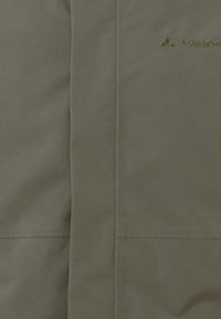 Grüne wasserfeste Jacke mit glatter Textur, minimalistischem Design und dezentem Branding. Enthält stromlinienförmige Nähte entlang der Säume.