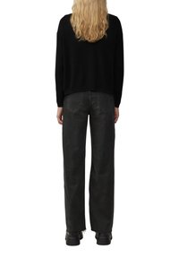Pull en maille noir avec une coupe décontractée et un col rond, associé à un jean gris à taille haute et jambes larges, et des bottes noires épaisses.