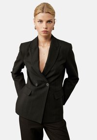 Sort blazer med smalstribet mønster og dyb V-udskæring, dobbeltbreasted knapper, strukturerede skuldre og to frontlommer. Glat stoftekstur.