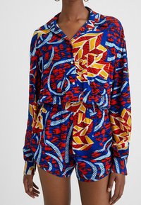 Buntes Set aus Hemd und Shorts mit blau, rot, gelb und weißen Blumenmustern. Lockere Passform, lange Ärmel und Knopfleiste.