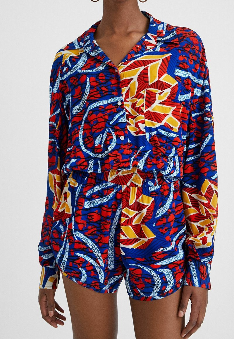 Buntes Set aus Hemd und Shorts mit blau, rot, gelb und weißen Blumenmustern. Lockere Passform, lange Ärmel und Knopfleiste.