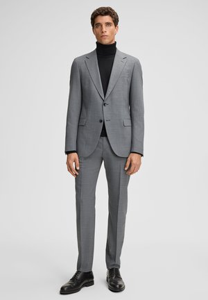 Gray suit with a checkered pattern, single-breasted jacket, notched lapels, and matching trousers. Worn with a black turtleneck and black shoes.