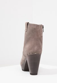 Brown suede ankle boot with a high wooden heel, featuring a side zipper and subtle stitch detailing along the edges.
