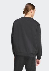 Μαύρο φούτερ με στρογγυλή λαιμόκοψη, φαρδιά εφαρμογή και ριμπ μανσέτες. Διακοσμητικό λευκό ρίγα κατά μήκος των ώμων. Απαλή υφή υφάσματος.