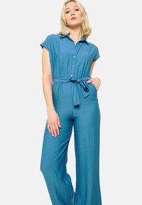 Turkizni kombinezoni s kratkimi rokavi, z ovratnikom, gumbi na sprednji strani in pasom. Iz lahkega materiala, s širokimi hlačnicami.