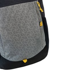 Rucksack aus grauen und schwarzen Stoffen mit einem geometrischen Muster, gelben Reißverschlussakzenten und einer strukturierten Oberfläche mit einem glatten Boden.