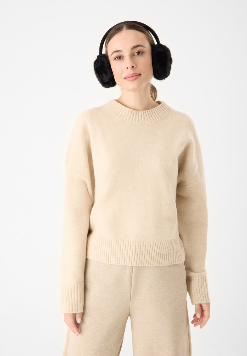 Beige gebreide trui met een geribde onderrand en mouwen, met een ronde halslijn. Gecombineerd met bijpassende beige broek. Zwarte bont oorwarmers.