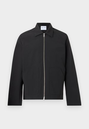 Μαύρο σακάκι με ευθεία σιλουέτα, μακριά μανίκια, μυτερό γιακά, κλείσιμο μπροστά με φερμουάρ και δύο μεγάλες τσέπες πατς. Λεία υφή υφάσματος.