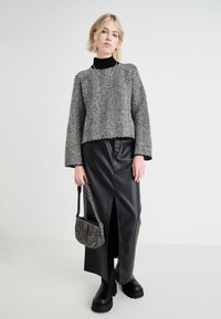 Maglione cropped con motivo a spina di pesce grigio e nero, abbinato a una gonna di pelle nera con uno spacco frontale. Stivali neri chunky e borsa piccola.