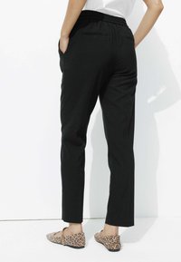 Pantalon noir ajusté avec taille élastique, doté de deux poches latérales et d'un tissu texturé. Assorti à des ballerines à pois.